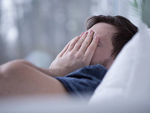 man in bed covering face tired in need of sleep apnea therapy