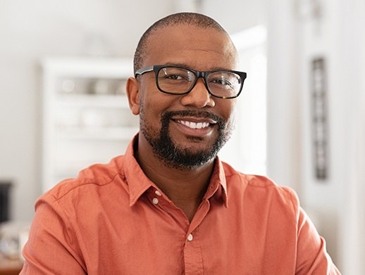man in orange shirt with glasses smiling after full mouth restoration