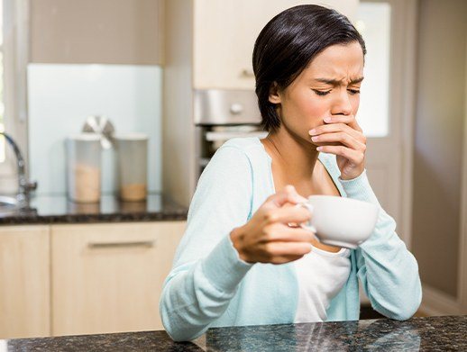 woman covering mouth while holding coffee cup in need of emergency dentistry