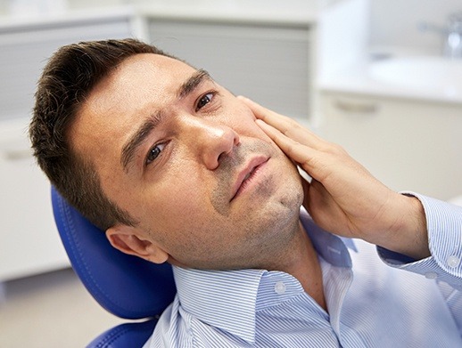 man laying back in pain holding cheek before emergency dentistry