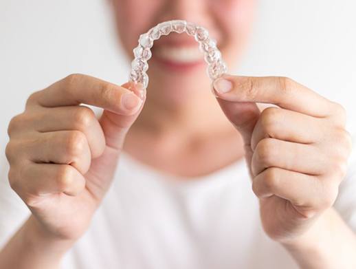 Smiling woman holding Invisalign in Skokie aligners in front of her