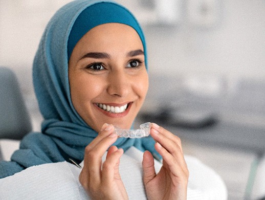 Woman smiling while holding Invisalign aligner