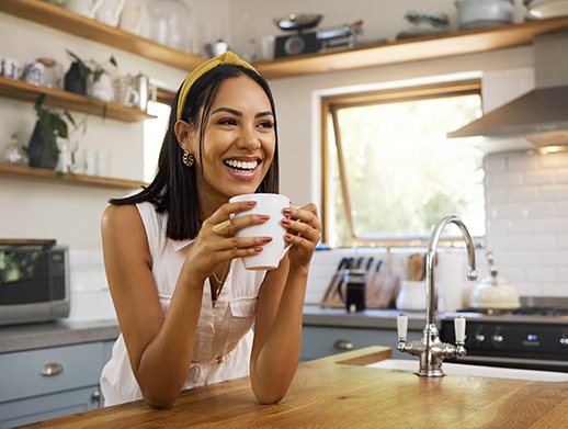 Woman smiling while drinking coffee in kitchen