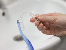 Patient using toothbrush to clean aligner