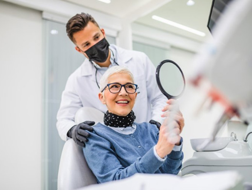 Dentist looking on as patient examines her dental implants in mirror 