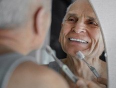 Man smiling in mirror as he brushes his teeth