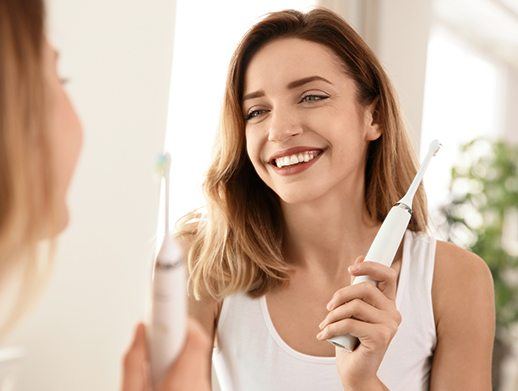 woman smiling in mirror while holding toothbrush