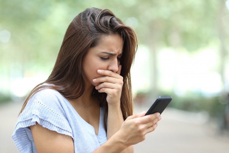 Woman covering her mouth while looking at her phone