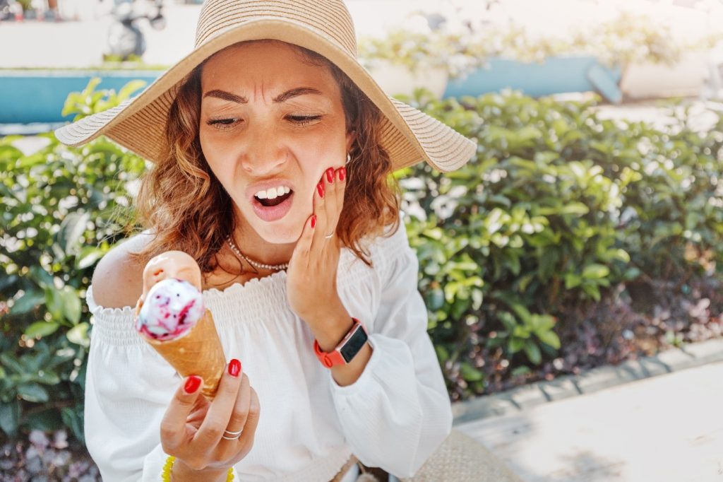 Woman experiencing a toothache while eating ice cream during summer vacation.