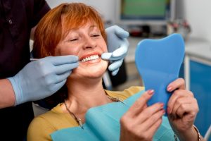 a woman is smiling at her dental implants in the mirror at the dentist