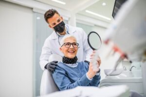 Woman standing in front of dentist looking at her teeth in a mirror.