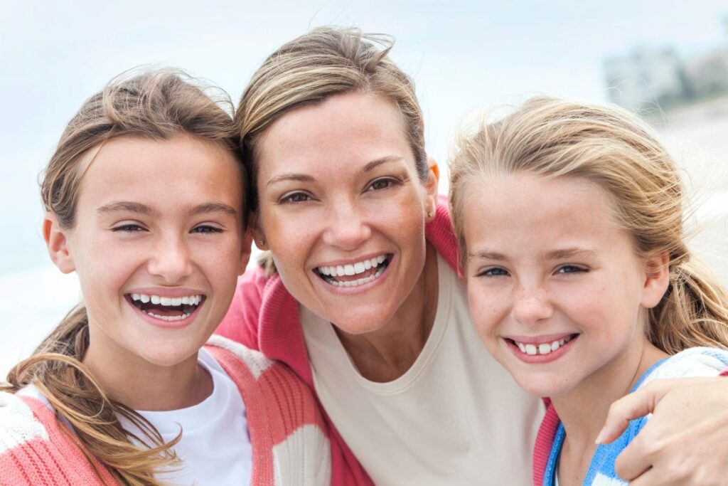 A mother and two children smiling on a beach.