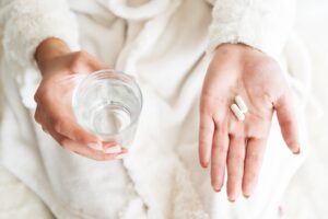 Two hands pictured, one holding pills and the other holding glass of water.